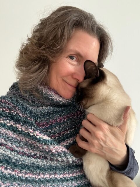 Maria Thomas wearing her Midnight Mountain Capelet and holding her pet Siamese cat.